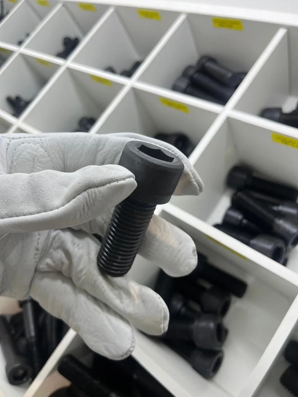 Parafuso sextavado preto em destaque, segurado com uma luva